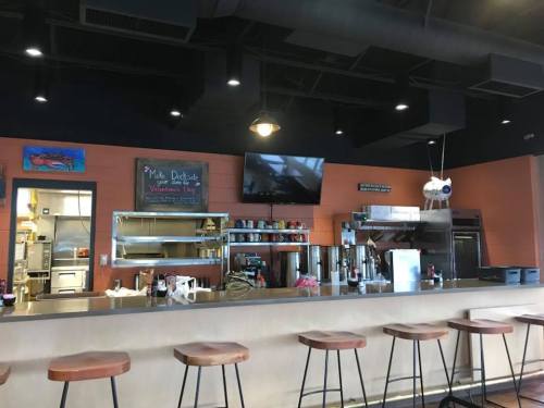 A modern café interior featuring a counter with stools, kitchen area, and a chalkboard menu on the wall.