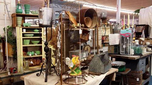 A vintage shop display featuring various antiques, kitchenware, and decorative items on tables and shelves.