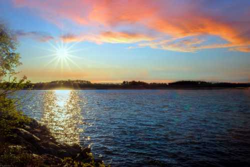 A serene sunset over a calm lake, with vibrant colors reflecting on the water and a starburst effect from the sun.