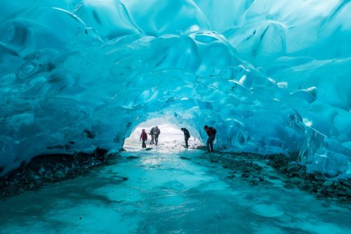 People exploring a stunning blue ice cave, with light filtering through the icy formations.