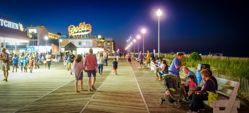 A lively boardwalk at night, with families walking, shops lit up, and people enjoying the seaside atmosphere.