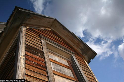 Close-up of a weathered wooden building against a blue sky with clouds, highlighting its rustic texture and details.