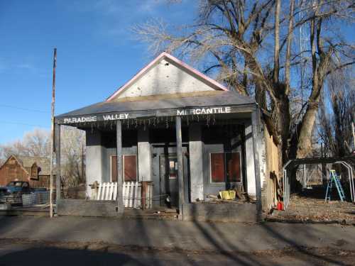 A weathered building with a sign reading "Paradise Valley Mercantile," surrounded by trees and a quiet street.