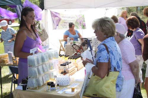 A vendor at a market displays skincare products while engaging with a customer at a booth.