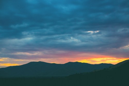 Silhouetted mountains against a colorful sunset sky with clouds.