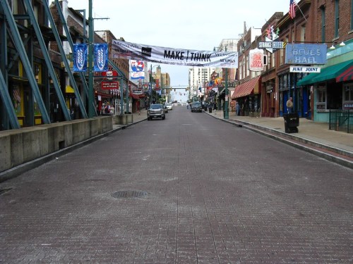 A wide street lined with shops and banners, empty of people and cars, under a clear sky.