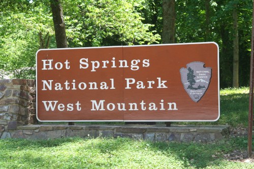 Sign for Hot Springs National Park, West Mountain, featuring the National Park Service logo and surrounded by greenery.