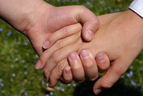 Two hands clasped together, symbolizing connection and unity, against a blurred green background.