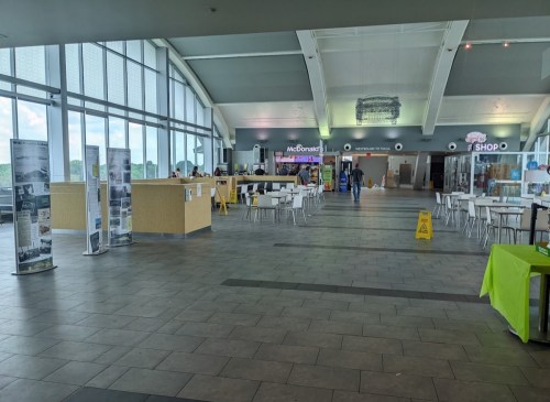 Interior of a spacious food court with seating, McDonald's, and informational displays. Caution sign visible on the floor.