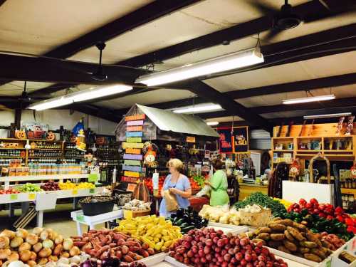 A vibrant market interior with colorful produce, shelves of jars, and shoppers browsing among fresh fruits and vegetables.