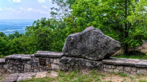 A large rock with "Jacob's Step" engraved, surrounded by greenery and a scenic view of the valley below.