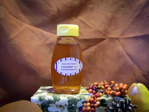 A bottle of lavender honey with a yellow cap, placed on a decorative box surrounded by grapes and a pear.