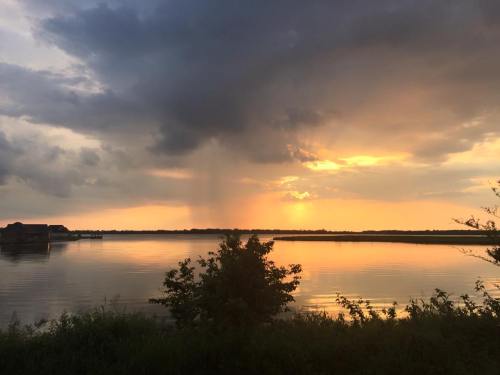 Sunset over a calm lake, with dark clouds and a hint of rain, reflecting warm colors on the water's surface.