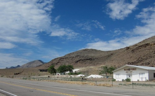 A rural landscape featuring a road, mountains, and a white building labeled "Mammoth Farms" under a cloudy sky.