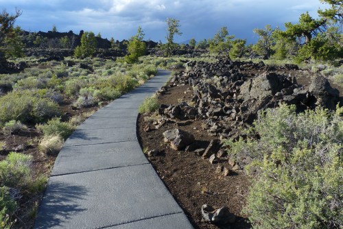 A winding pathway through a rocky landscape with sparse vegetation and trees under a cloudy sky.