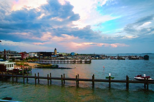 A scenic waterfront view with boats docked, colorful buildings, and a cloudy sky at sunset.