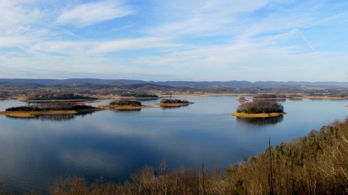 A serene landscape featuring a calm lake with several small islands and distant mountains under a blue sky.