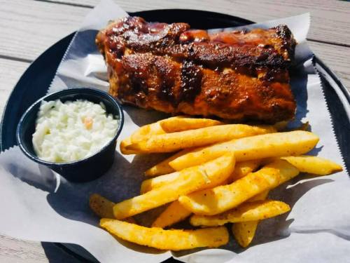 A plate with BBQ ribs, golden fries, and a side of coleslaw on a wooden table.