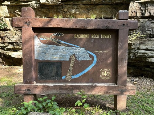 Sign for Backbone Rock Tunnel, featuring a map and information about Beaverdam Creek, set against a rocky background.