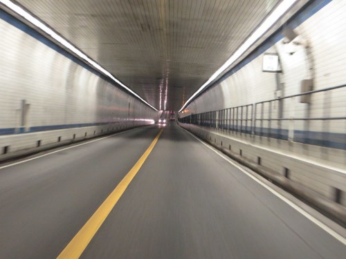 A blurred view of a tunnel with white tiled walls and yellow lane markings, creating a sense of motion.