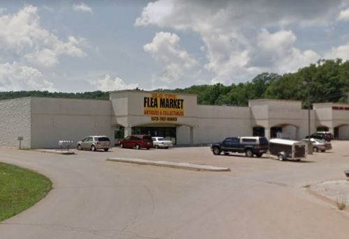 Exterior view of a flea market building with a large sign, surrounded by parked cars and a cloudy sky.