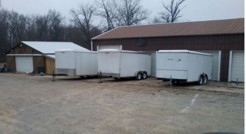 Three white trailers parked next to a brown storage building on a gravel lot, with trees in the background.