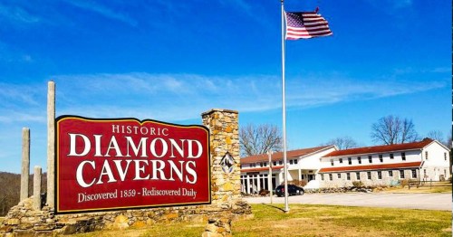 Sign for Historic Diamond Caverns with an American flag and a clear blue sky in the background.