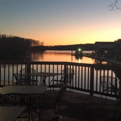 A serene sunset over a calm lake, with silhouettes of trees and a dock in the foreground.
