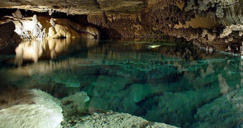 A serene underground cave with clear water reflecting the rocky ceiling and walls, illuminated by soft lighting.