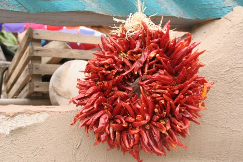 A vibrant wreath made of dried red chili peppers hanging against a textured wall.
