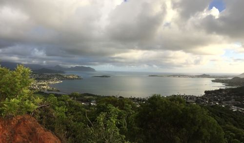 A panoramic view of a coastal landscape with mountains, water, and clouds under a partly cloudy sky.