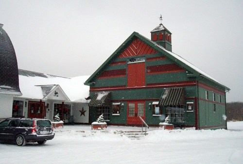 A green and red barn-style building covered in snow, with a bell tower and steps leading to the entrance.