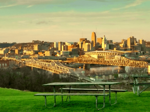 A city skyline at sunset, featuring bridges and green grass in the foreground.