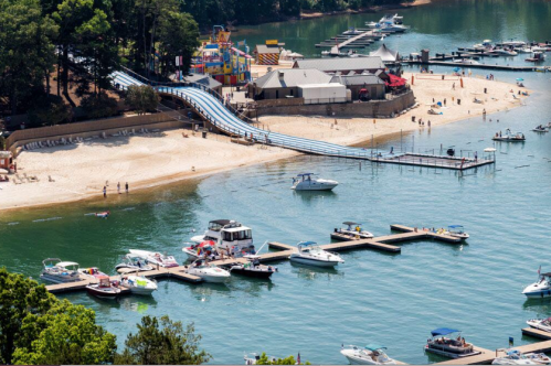 Aerial view of a beach with water slides, boats docked, and people enjoying the sunny day by the water.