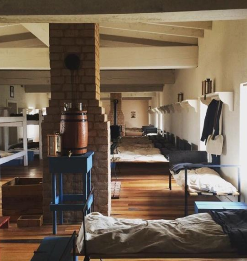 Interior of a dormitory with wooden beds, blue furniture, and a brick column, creating a rustic, communal atmosphere.