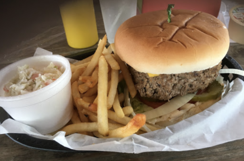 A plate with a burger topped with cheese, lettuce, and pickles, served with fries and a side of coleslaw.