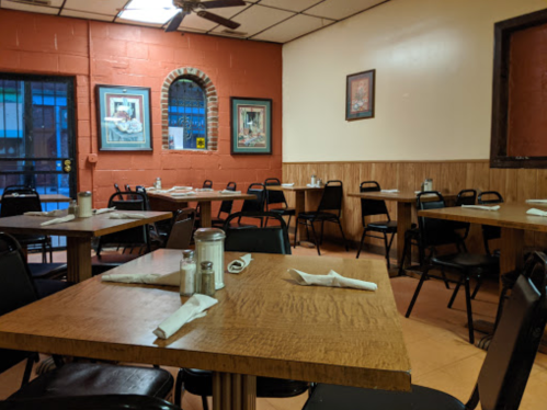 A cozy restaurant interior with wooden tables, black chairs, and framed artwork on the walls.
