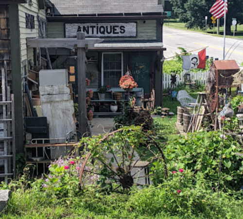 A quaint antique shop with a garden, featuring vintage items and colorful flowers in a rural setting.
