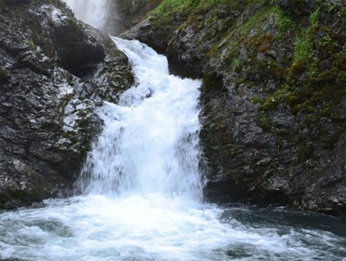 A cascading waterfall flows over rocky terrain, surrounded by lush greenery.