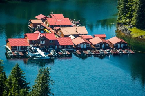 A cluster of floating cabins with red roofs on a serene blue lake, surrounded by lush greenery.