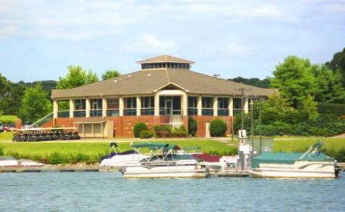 A lakeside building with a large porch, surrounded by greenery and boats docked in the water.