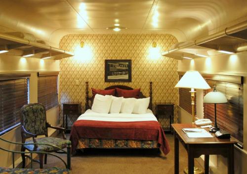 Cozy train cabin featuring a double bed, decorative wallpaper, a lamp, and a small desk with a chair.