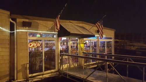 A brightly lit restaurant entrance at night, featuring American flags and an "Open" sign.