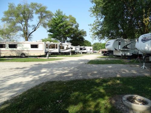 A gravel path leads through a campground with several parked RVs and trees in the background under a clear blue sky.