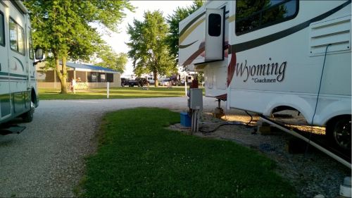 A view of an RV park with two RVs parked on a gravel path, surrounded by trees and grassy areas.