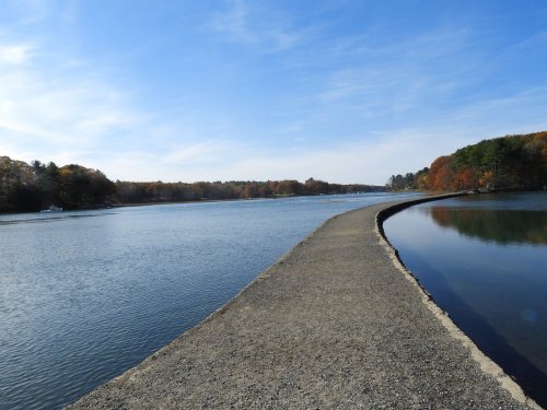 A serene river scene with a winding path along the water, surrounded by autumn foliage and a clear blue sky.