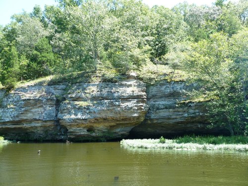 A serene river scene featuring a rocky cliff surrounded by lush greenery and calm water.