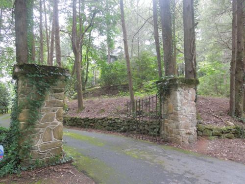 Stone gateposts covered in ivy, leading to a wooded path surrounded by tall trees and greenery.