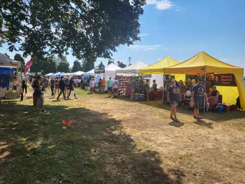 A sunny outdoor market scene with various vendor tents and people browsing among the stalls.