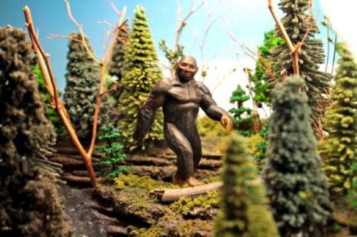 A miniature Bigfoot figure walking through a dense forest scene with trees and greenery.